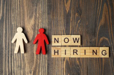 Wooden figure and wooden cubes with Now Hiring letters on a wooden background. Human resources management concept