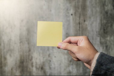 A business hand holding a piece of empty notepaper on a blurred background. Empty notepaper for copy space