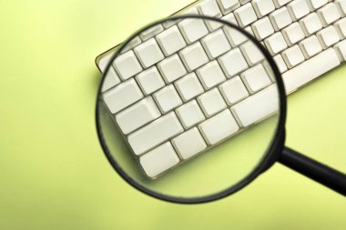 A closeup view of a magnifying glass focuses on a computer keyboard button on a colored background