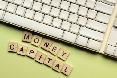 Closeup view of computer keyboard and a row of wooden cubes with MONEY CAPITAL letters. The financial and economic concept