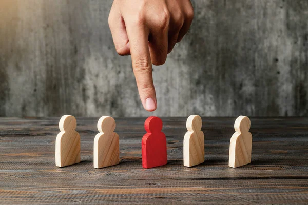A human hand pointing a red wooden figure from the row of wooden figures on a wooden table. Leadership concept