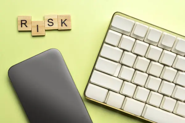 Closeup view of a computer keyboard with a mobile phone with a blank screen and a wooden cube with a risk letter. Risk management concept