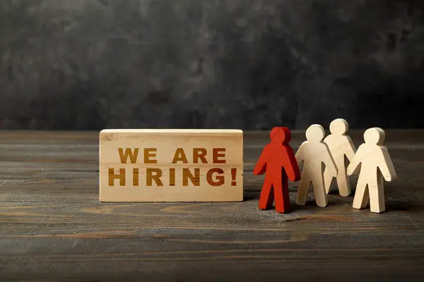 Wooden figure and wooden cubes with We Are Hiring letters on a wooden background. Human resources management concept