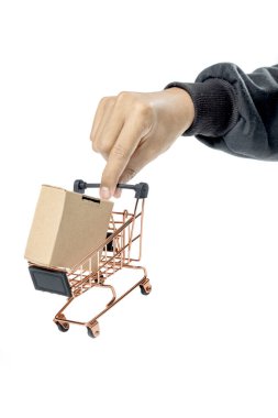 İnsan eli, beyaz bir arka planda izole edilmiş bir alışveriş arabasında karton bir kutu taşır.