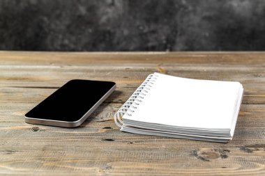 Boş ekranlı cep telefonunun yakın görüntüsü ve ahşap arka planda boş bir defter. Boş cep telefonu ekranı ve kopyalama alanı için boş defter