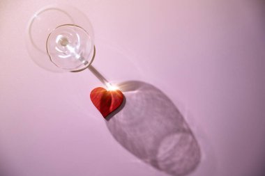 Pembe arka planda kırmızı kalpli şarap kadehi. Romantik akşam yemeği Sevgililer Günü konsepti