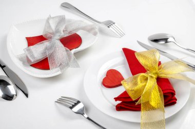 Çatal, bıçak ve kırmızı kalp ve kurdeleli kaşık takımları beyaz arka planda izole edilmiş. Romantik akşam yemeği Sevgililer Günü konsepti