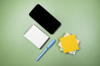 Boş ekranlı cep telefonunun yakın görüntüsü ve renkli bir arkaplan üzerine boş bir defter ve not kağıdı. Boş cep telefonu ekranı ve kopyalama alanı için not kağıdı içeren boş bir defter