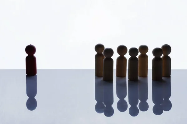 Closeup view of a red wooden figure standing with a crowd of brown wooden figures on a white background. Human resources management concept