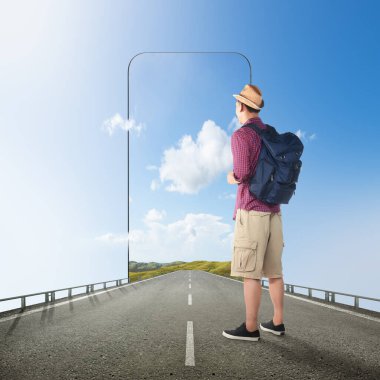 Sırt çantalı Asyalı bir adam cep telefonu ekranında tepe manzaralı bir sokakta duruyor. Seyahat kavramı