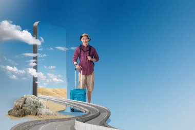 Sırt çantalı Asyalı bir adam cep telefonu ekranında çöl manzaralı bir bavul taşıyor. Seyahat kavramı