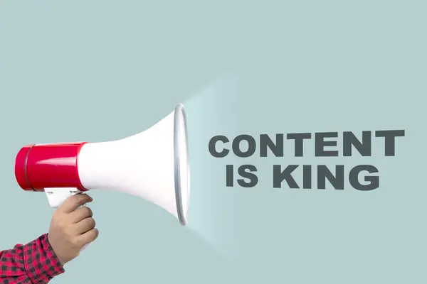 A human hand holding a megaphone with content is king text on a colored background. Content manager, strategy and creativity concept