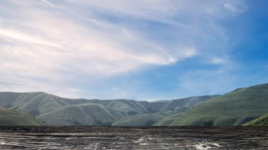 Ahşap zemin, dağ manzaralı, mavi gökyüzü arka planlı.