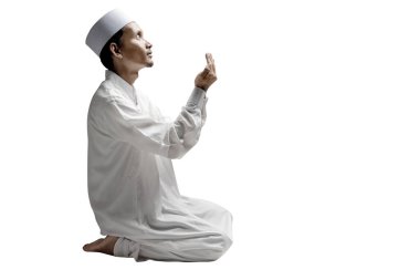 Müslüman bir adam oturur, ellerini kaldırır ve beyaz bir arkaplanda yalnız başına Allah 'a dua eder.
