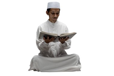 Müslüman bir adam beyaz bir arkaplanda oturmuş Kuran okuyor.