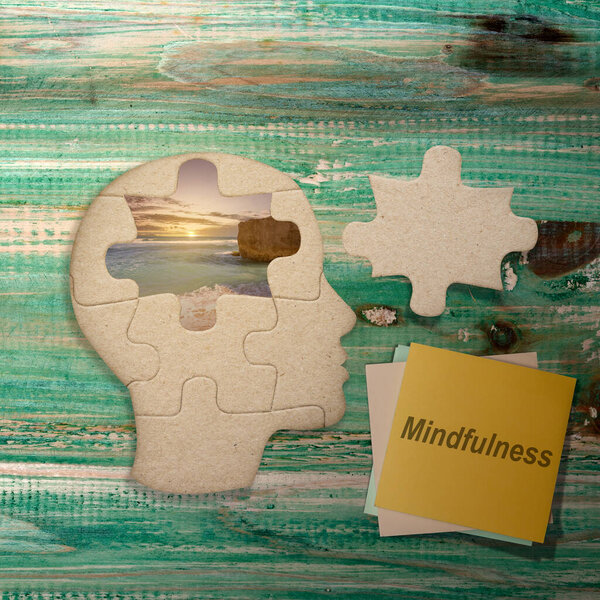 Stack of paper with mindfulness text and missing piece of the head puzzle with a nature view on the table. Health mindfulness concept