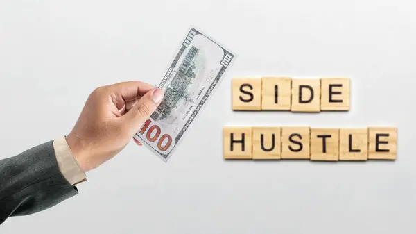 Man's hand holding dollars in his hands with text from wooden cubes side hustle isolated over white background. Side hustle or side job income.