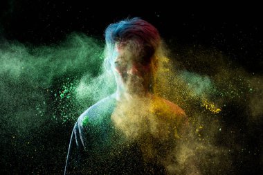 Asyalı adam renkli holi tozu sıktı ve siyah arka planda izole edilmiş eğleniyor. Renk festivali Hindistan konsepti.