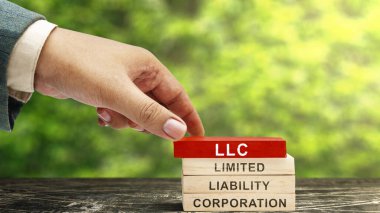 İş adamı, üzerinde LLC yazıları olan bir yığın tahta blok yerleştirdi. Limited Limited Borbility Company 'nin kısaltması. İş konsepti