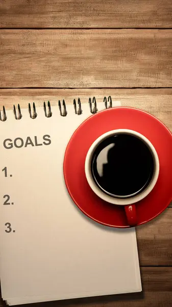 A notebook with goals list text and a cup of coffee on the table. Planning and target concept