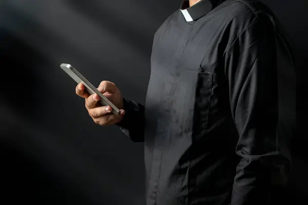 黒い背景に携帯電話を使用した牧師の肖像画 キリスト教コンセプト ストック写真