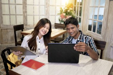 İki mutlu genç iş adamı bir kafede görüntülü görüşme yapıyorlar. İki Endonezyalı neşeli girişimci birlikte çalışıyor ve online toplantıya katılıyor. 