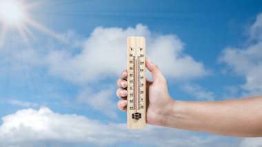 Sıcak ve gökyüzü arkaplanı olan termometreyi tutan insan eli. Çevre, küresel ısınma ve iklim değişikliği kavramı