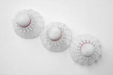 Kırmızı detaylarla beyaz bir yüzeye dizilmiş üç beyaz badminton mekiği sporla ilgili makaleler ve promosyon materyalleri için uygun bir minimalist tasarım yaratıyor.