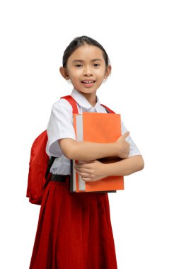 Sırt çantalı Asyalı bir ilkokul öğrencisinin portresi beyaz bir arkaplan üzerinde izole bir kitap tutarken.