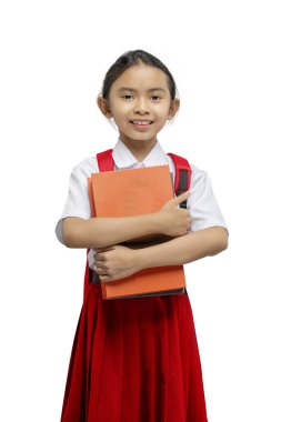 Sırt çantalı Asyalı bir ilkokul öğrencisinin portresi beyaz bir arkaplan üzerinde izole bir kitap tutarken.