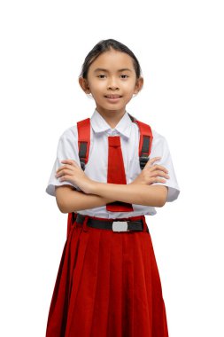 Asyalı bir ilkokul öğrencisinin portresi üniformalı, sırt çantalı, kolları çaprazlanmış beyaz bir arka plan üzerinde duruyor.