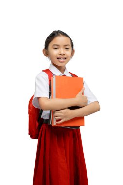 Sırt çantalı Asyalı bir ilkokul öğrencisinin portresi beyaz bir arkaplan üzerinde izole bir kitap tutarken.