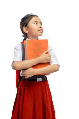 Kırmızı etekli, okul üniformalı genç bir kız, beyaz bir arka planda, düşünce ve arzu ifadesiyle yukarıya bakarken göğsüne yakın turuncu bir ders kitabı tutuyor.