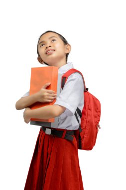 Kırmızı sırt çantalı neşeli genç kız yukarı bakıyor, elinde turuncu bir kitap var. Kırmızı etekli, beyaz bir okul üniforması içinde yeni bir öğrenme gününe hazır.