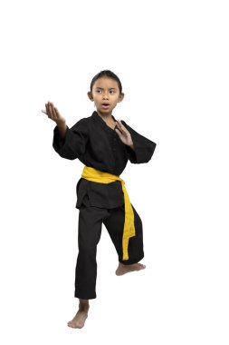 Sarı kuşaklı odaklanmış bir çocuk, geleneksel siyah giyerek, beyaz bir arka planda izole edilmiş, dövüş sanatları eğitiminde disiplin ve kararlılık gösteren bir karate duruşu sergiliyor.