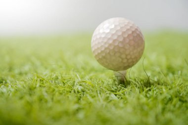 Beyaz bir golf topunun detaylı yakın plan çekimi, canlı yeşil çimenlerin üzerine tünemiş, yumuşak, odaklanmamış bir arka plana kurulmuş, sporda rahatlık ve hassasiyet aktarıyor.