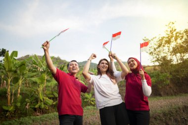 Endonezyalı insanların portresi. Heyecanlı ifadeleri var. Açık havada mavi gökyüzü arka planında küçük Endonezya bayrakları tutuyorlar.