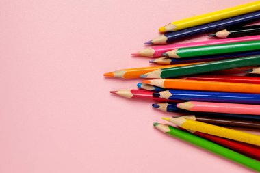 Pembe arka planda renkli kalemler var. Kalemler aynı yöne bakacak şekilde dizilmiş, düzen ve düzen duygusu yaratıyorlar.