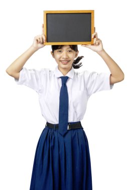Beyaz ve mavi üniformalı Asyalı bir ortaokul öğrencisinin portresi beyaz arka planda izole edilmiş küçük boş tahtayı gösteriyor.