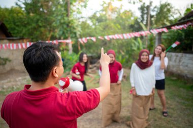 Kırmızı gömlekli bir adam megafon tutuyor ve oyun oynayan bir grup insanı işaret ediyor. Endonezya 'nın bağımsızlık günü kavramı