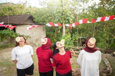 Bir grup kadın sürüngen yeme yarışması yapıyor. Bayraklar kırmızı ve beyaz. Kadınlar gülümsüyor ve eğleniyorlar. Endonezya 'nın bağımsızlık kavramı