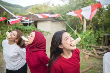 Bir grup kadın sürüngen yeme yarışması yapıyor. Bayraklar kırmızı ve beyaz. Kadınlar gülümsüyor ve eğleniyorlar. Endonezya 'nın bağımsızlık kavramı