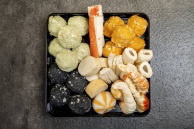 İçinde yengeç ve yeşil top da dahil olmak üzere çeşitli yiyecek malzemelerinin bulunduğu siyah bir tepsi. Tepsi gri bir yüzeye yerleştirildi.