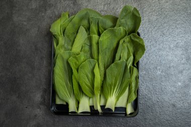 Bir tepsi yeşil sebze, biraz brokoli de dahil, tezgahın üzerinde duruyor. Sebzeler taze ve sağlıklı ve lezzetli görünüyorlar. Tepsi siyah ve parlak.