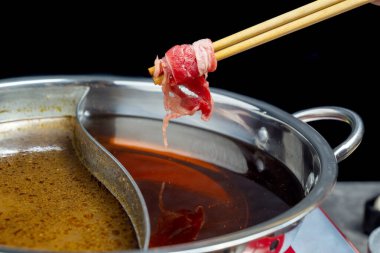 Bir insan tavadaki bir et parçasını yemek için çubuk kullanıyor. Tava kırmızı sosla dolu ve et pişiyor.