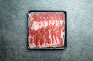 Bir tepsi et gri bir yüzeyde. Et dilimlenir ve kare şeklinde dizilir.