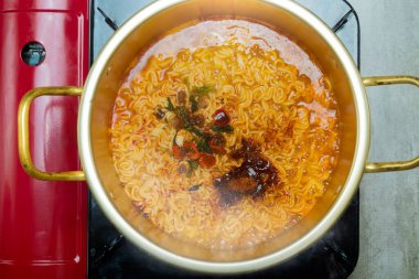 Fırında bir tencere hazır şehriye pişiriliyor. Erişteler kırmızı kasede, tencere de kırmızı ocağın üstünde.