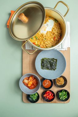 Tahtanın tepesinde kapağı olan bir kap hazır şehriye ve birkaç kase yiyecek ve sos.