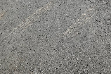 Beyaz çizgili gri ve siyah bir kaldırım. Asfalt betondan yapılmış ve pürüzlü bir dokusu var.