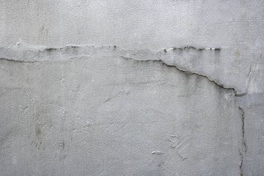 Çatlak ve delikli gri bir duvar. Duvar betondan yapılmış ve pürüzlü bir dokusu var.